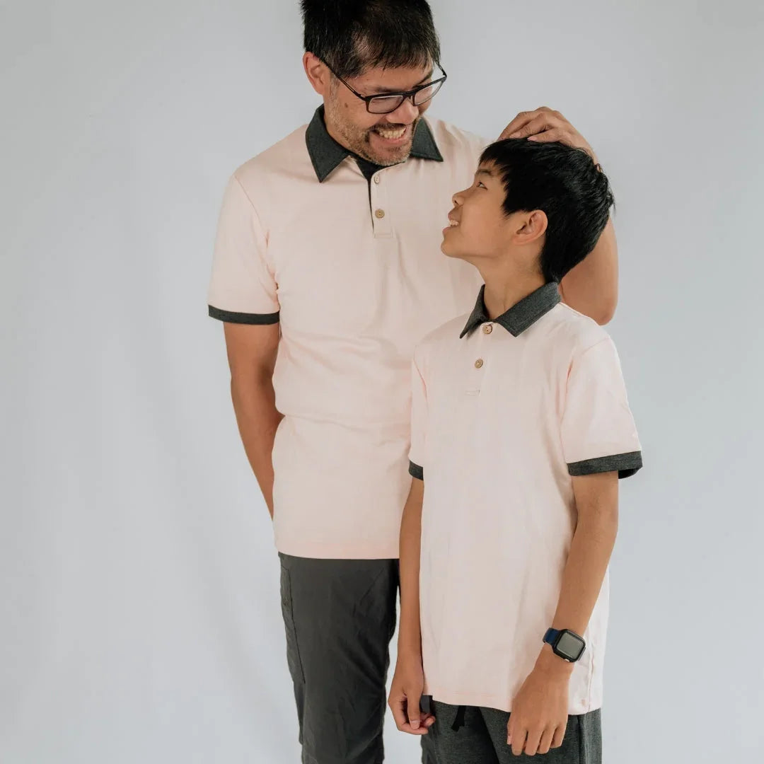 Father and son in matching light pink polo shirts with dark collars, smiling indoors