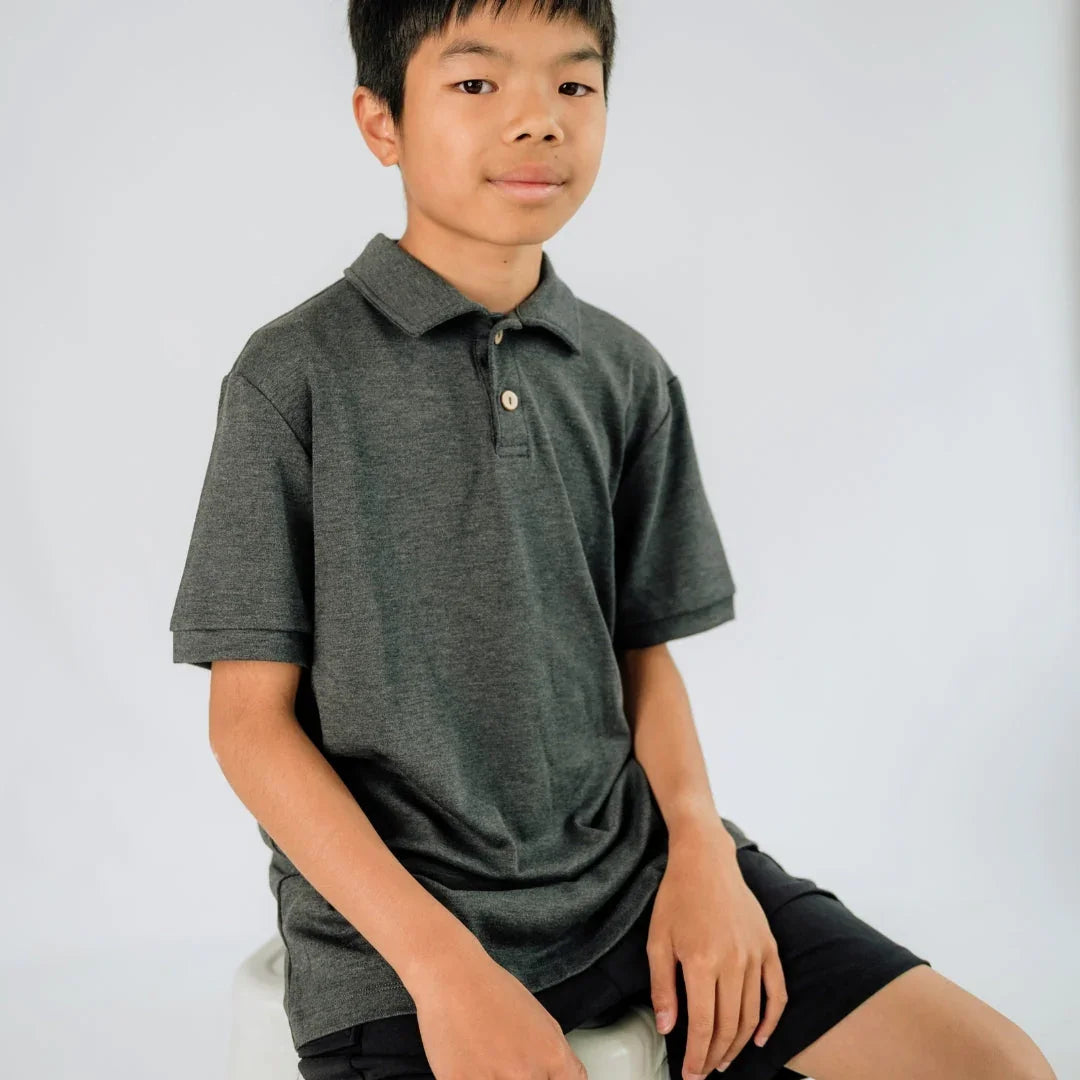 Youth wearing dark grey polo shirt sitting on stool, plain background