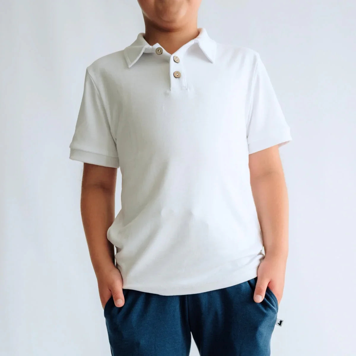 Boy wearing white polo shirt with buttons and navy pants, standing against white background