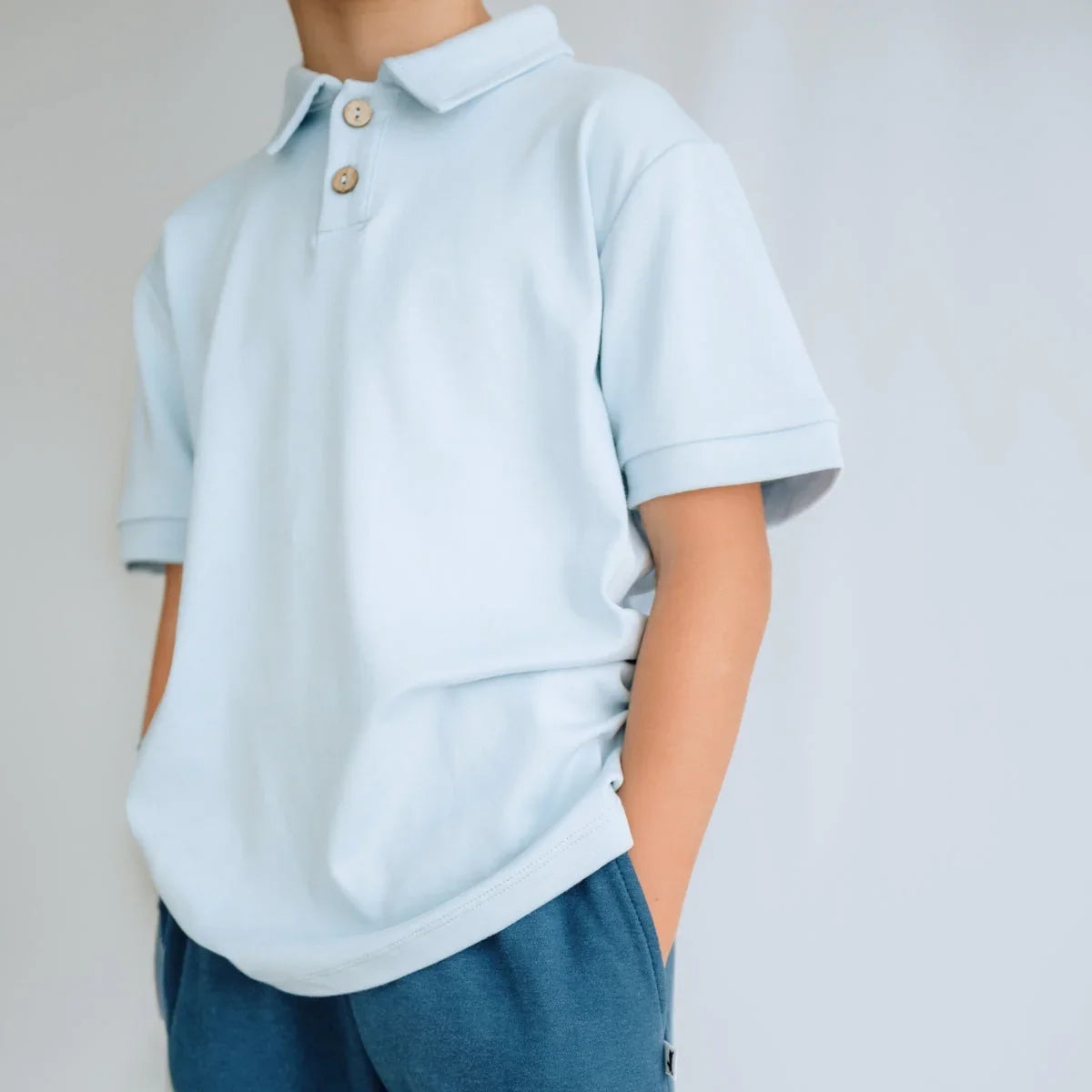 Child wearing light blue polo shirt with wooden buttons and blue shorts