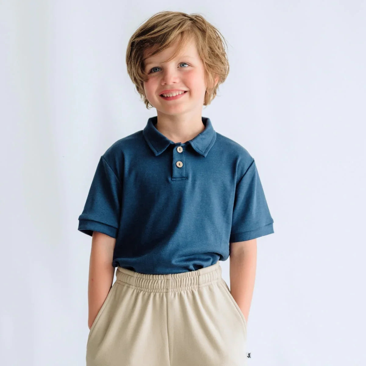 Smiling boy in blue polo shirt and beige pants against plain white background