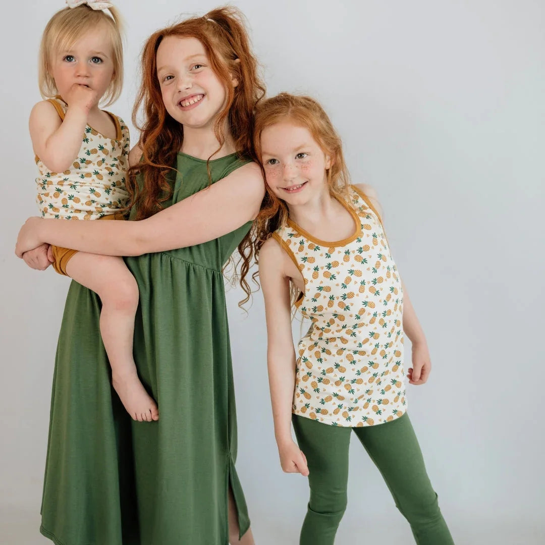 Three smiling children in matching green and pineapple print outfits against a plain background