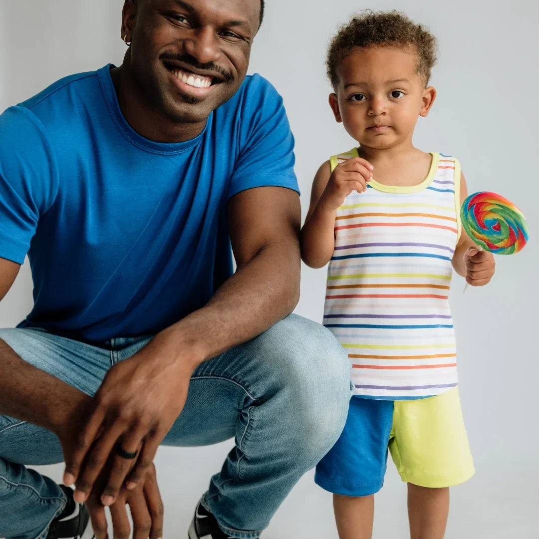 Smiling man in blue shirt with child in striped tank and shorts holding rainbow lollipop