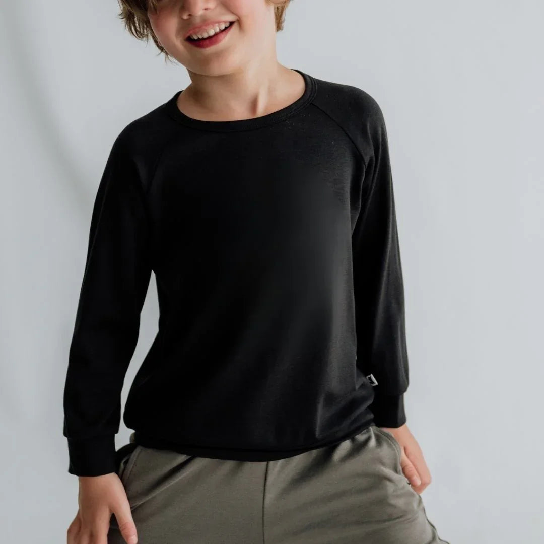 Smiling child in black long-sleeve shirt and khaki pants against light gray background