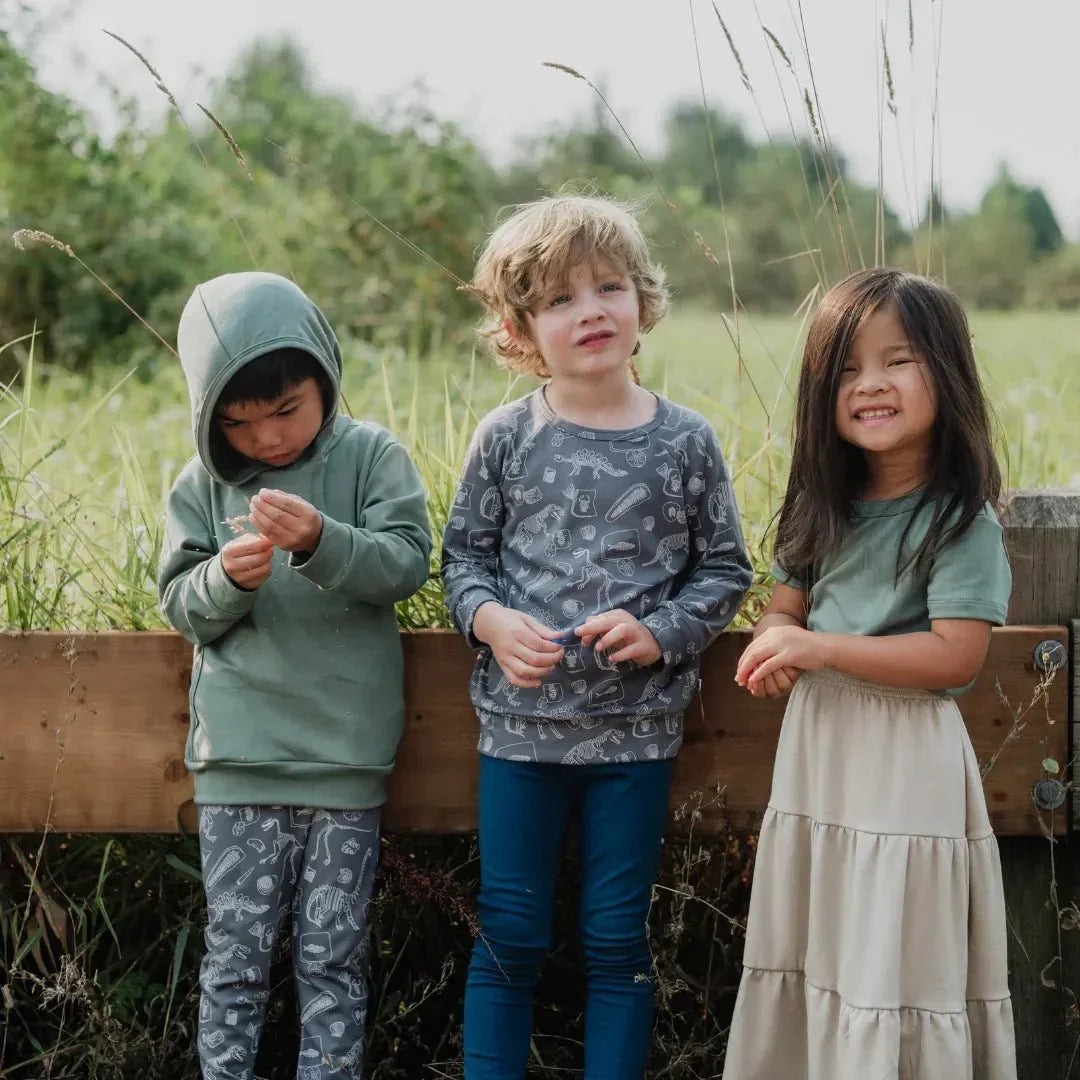 Three kids in bamboo pullover prints and leggings outdoors by a wooden fence