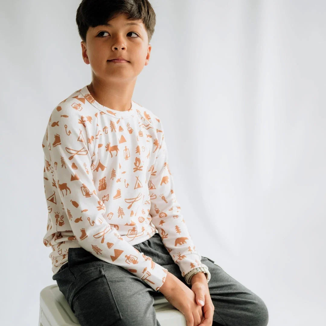 Youth wearing white printed pullover with camping icons, casual grey pants, studio background