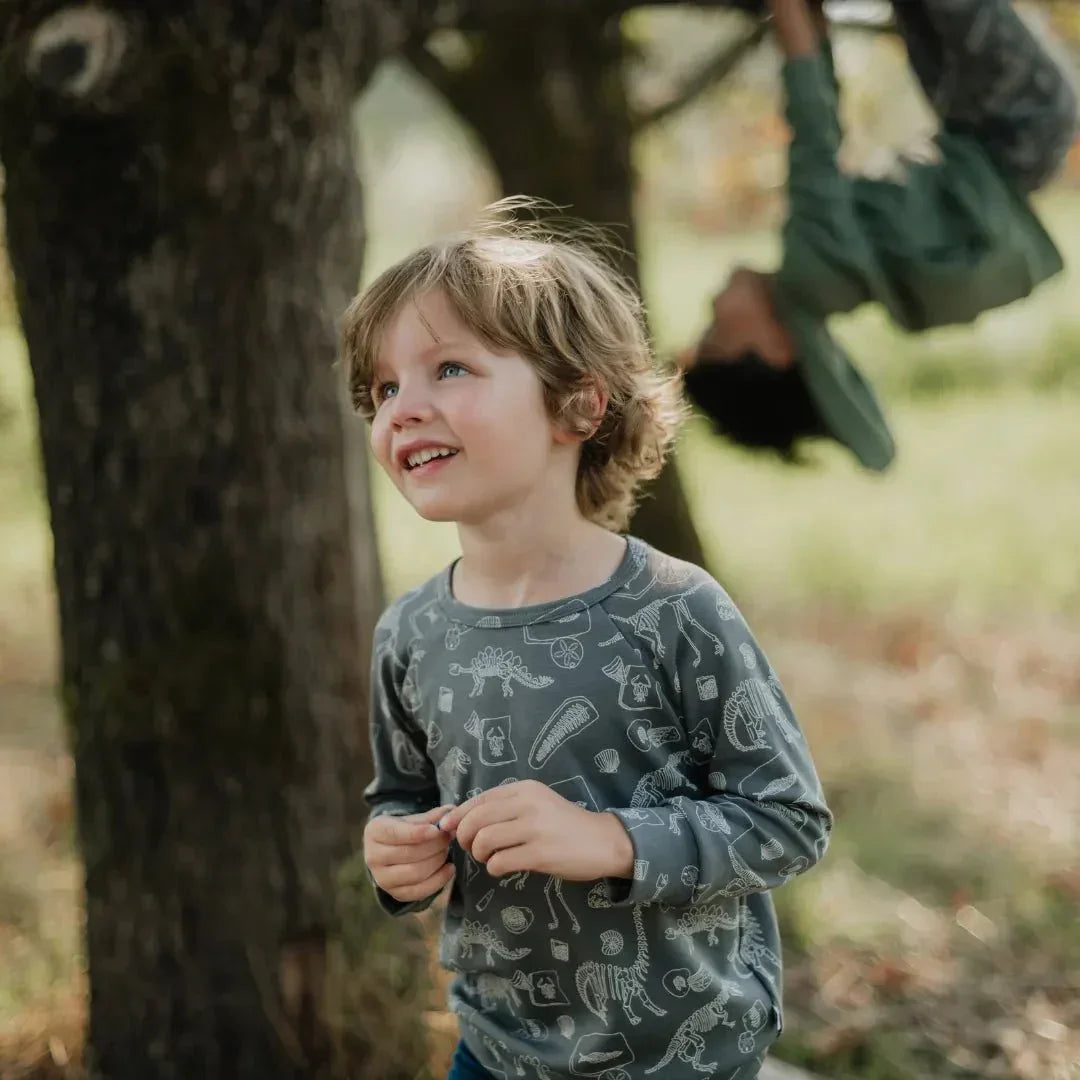 Young boy in printed bamboo raglan pullover outdoors by a tree, smiling in nature