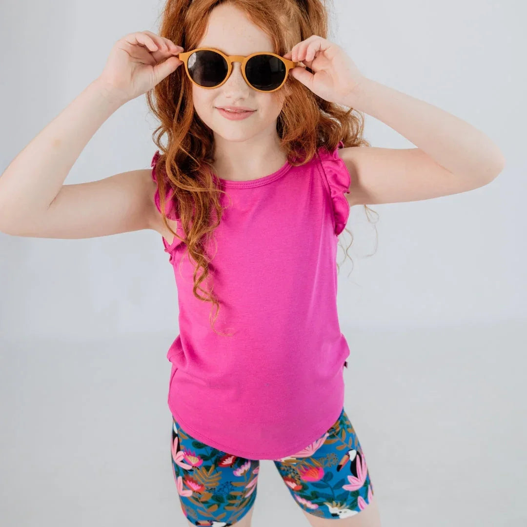 Girl in pink ruffle sleeve top, floral shorts, and sunglasses posing in studio