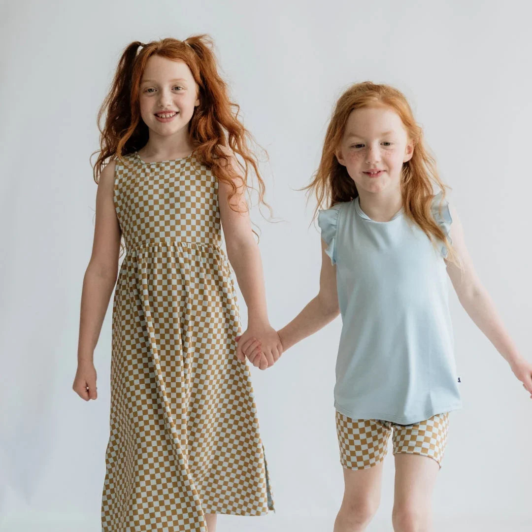 Two red-haired girls in checkered brown and white outfits holding hands, studio background