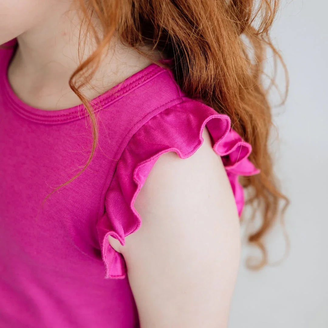 Girl with red hair wearing a pink ruffle sleeve top, close-up on shoulder