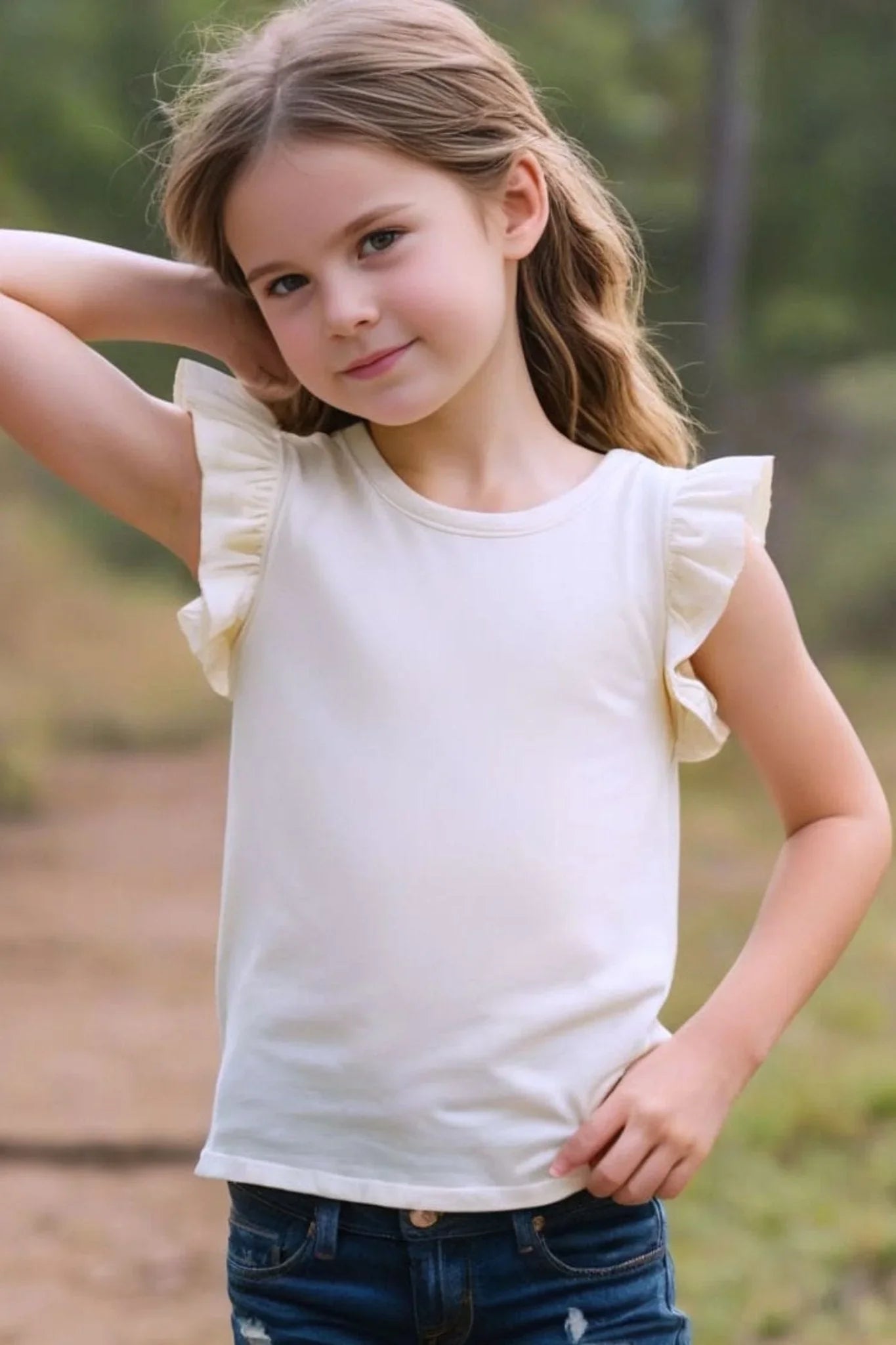 Girl wearing cream bamboo ruffle tank top and jeans outdoors, kids summer fashion