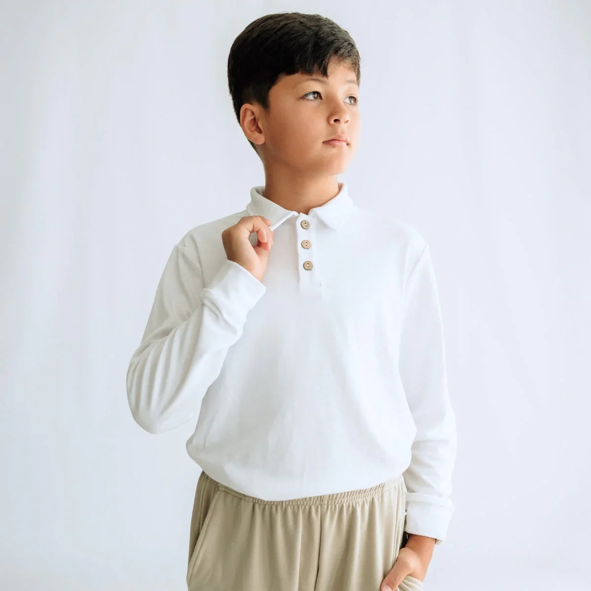Boy in white long sleeve polo shirt and beige pants on plain background