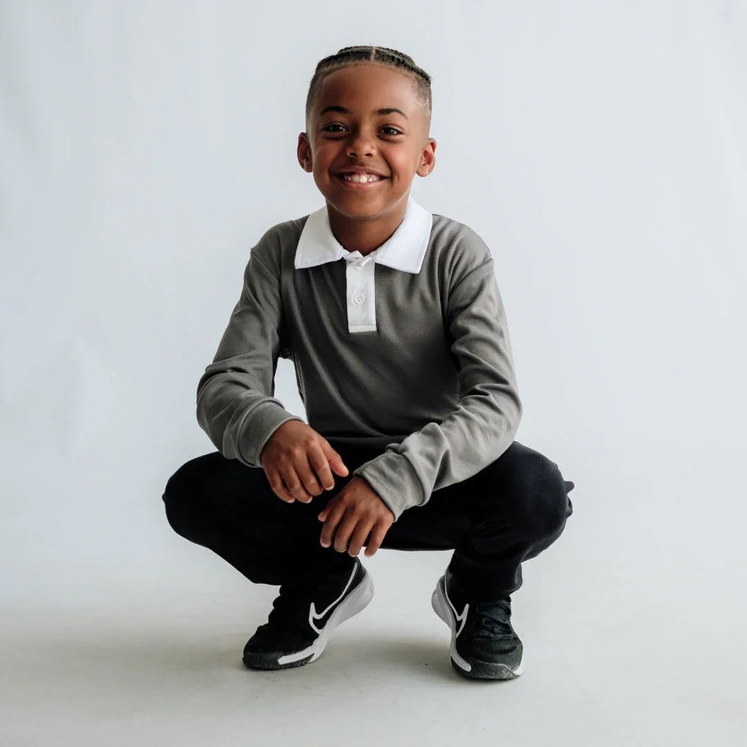 Smiling boy posing in gray polo shirt, black pants, and Nike sneakers in studio setting