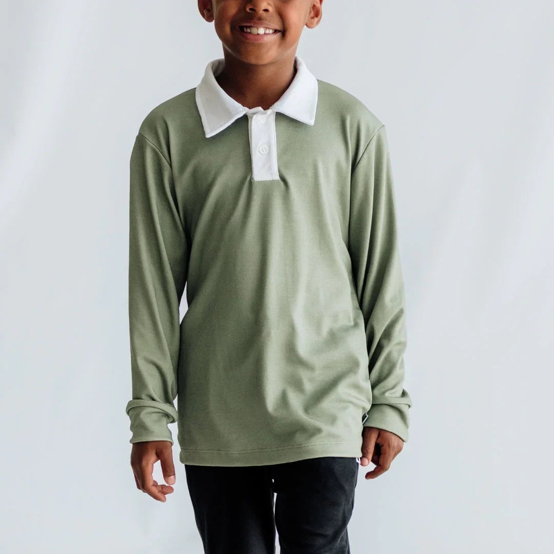 Smiling child wearing sage green long sleeve polo shirt with white collar, plain background