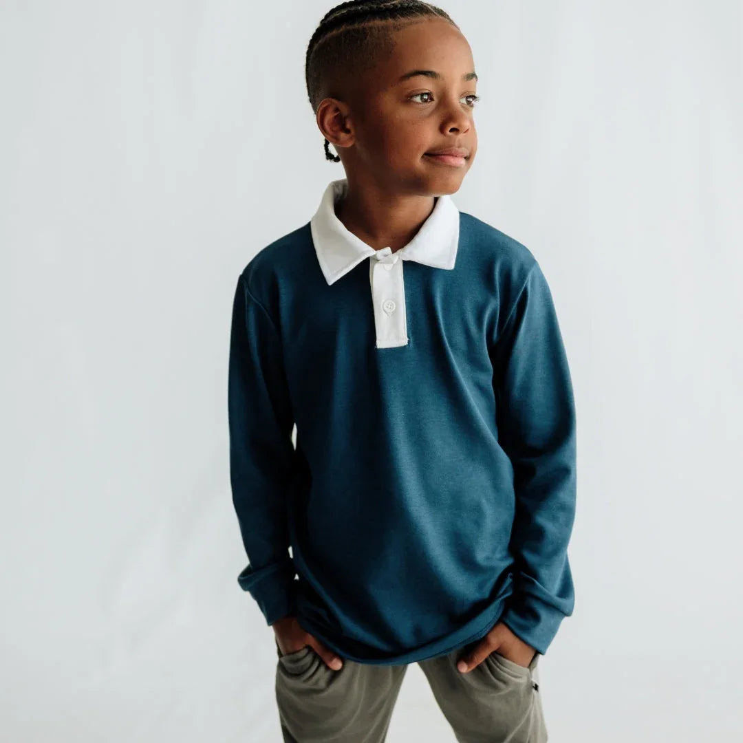 Smiling boy in blue long sleeve polo shirt with white collar against light background