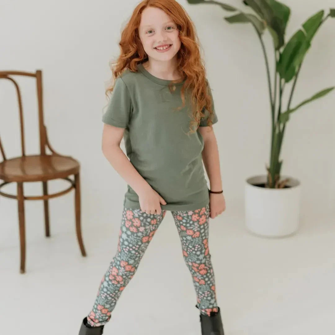 Smiling child in green bamboo t-shirt and floral leggings in bright indoor setting