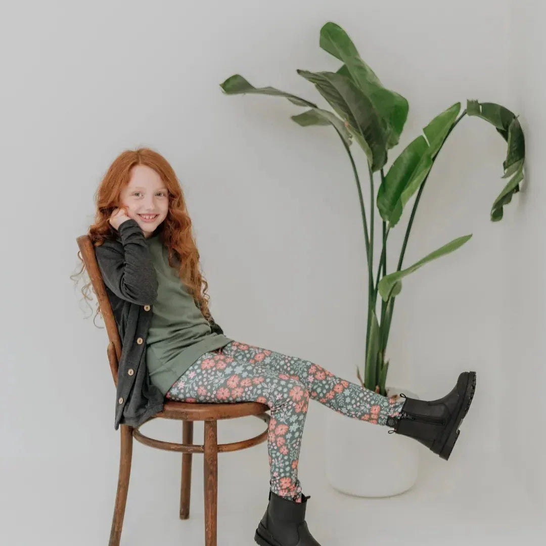 Girl in bamboo t-shirt and floral leggings sitting on chair with green plant background