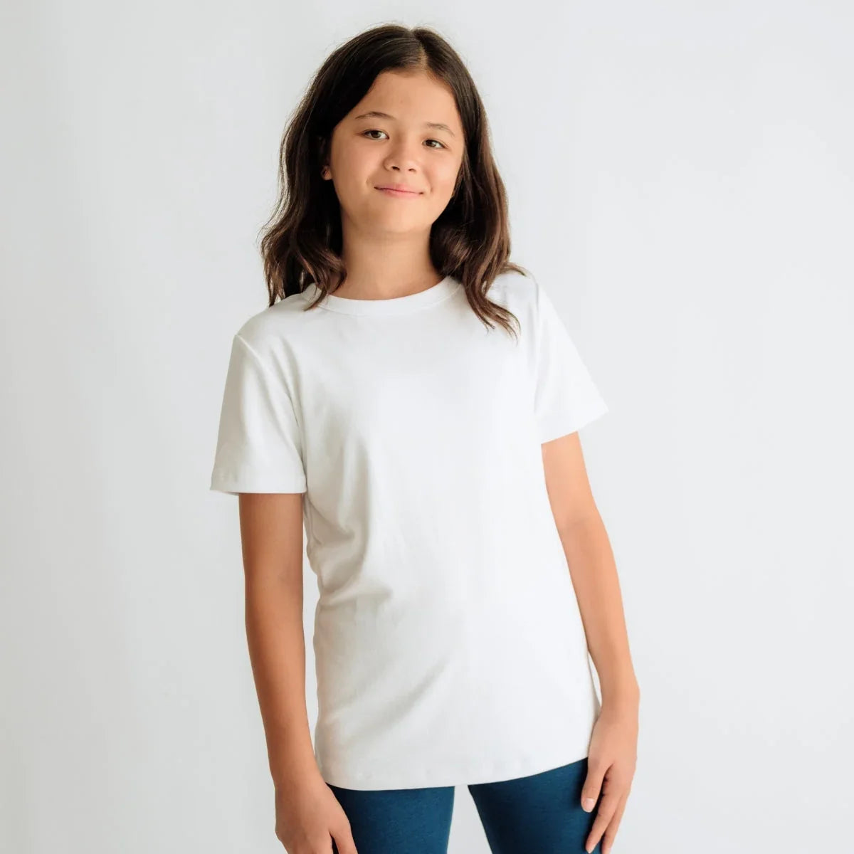 Smiling child wearing plain white t-shirt and blue leggings against white background