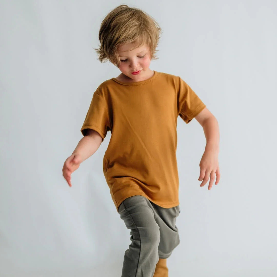 Young child in mustard yellow t-shirt and gray pants posing against light background