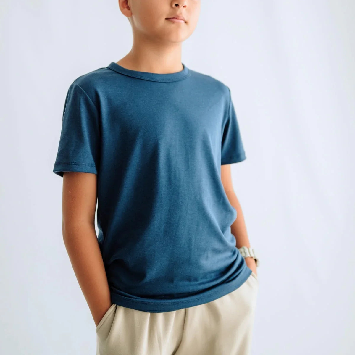 Boy wearing blue t-shirt and beige shorts with hands in pockets, plain background