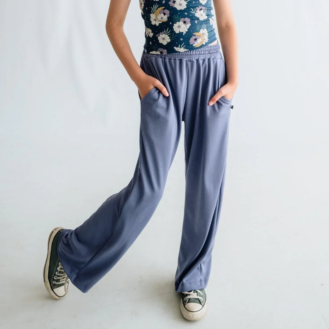 Girl in relaxed blue lounge pants, floral top, and sneakers standing in studio setting