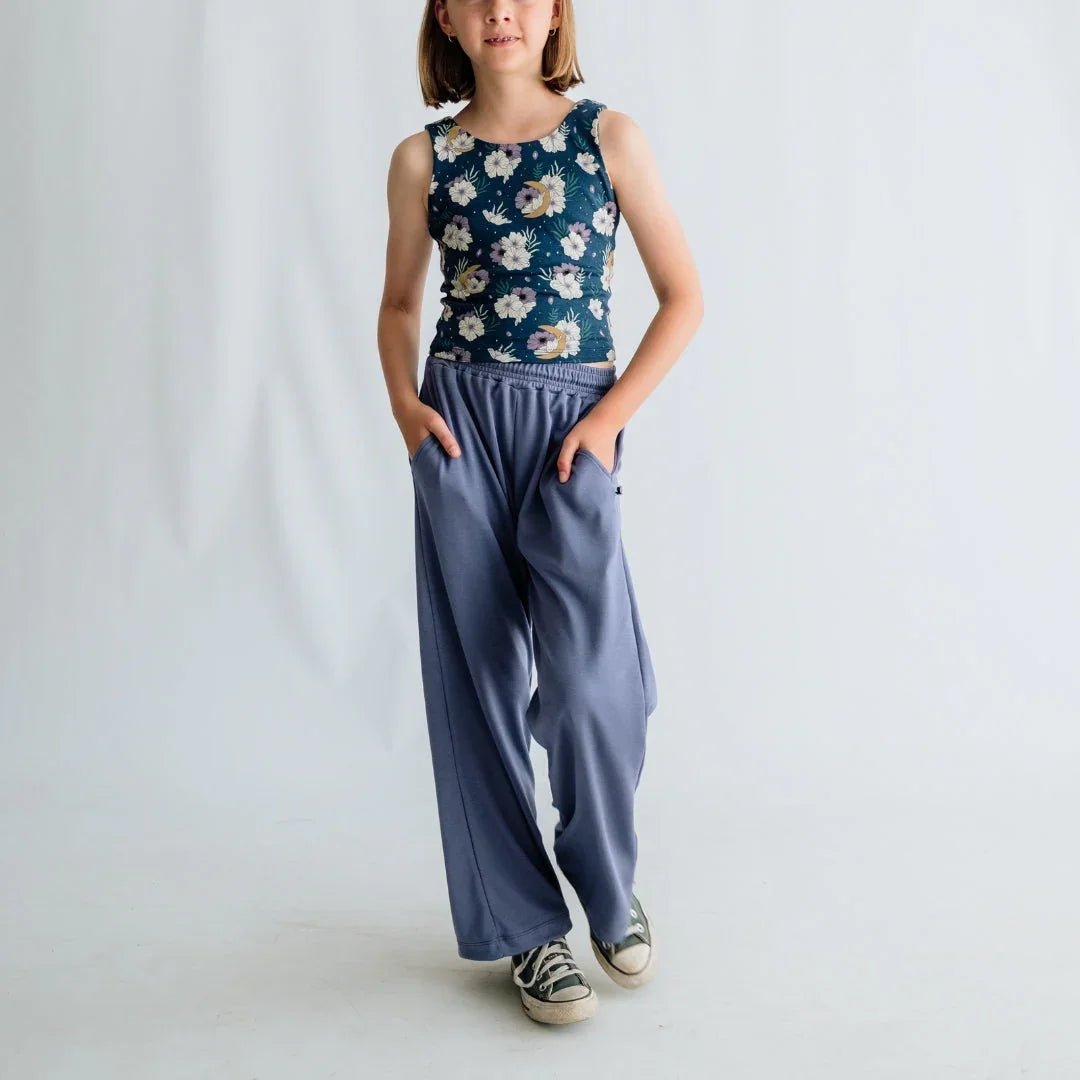 Girl in floral tank top and loose blue pants with sneakers, posing in studio