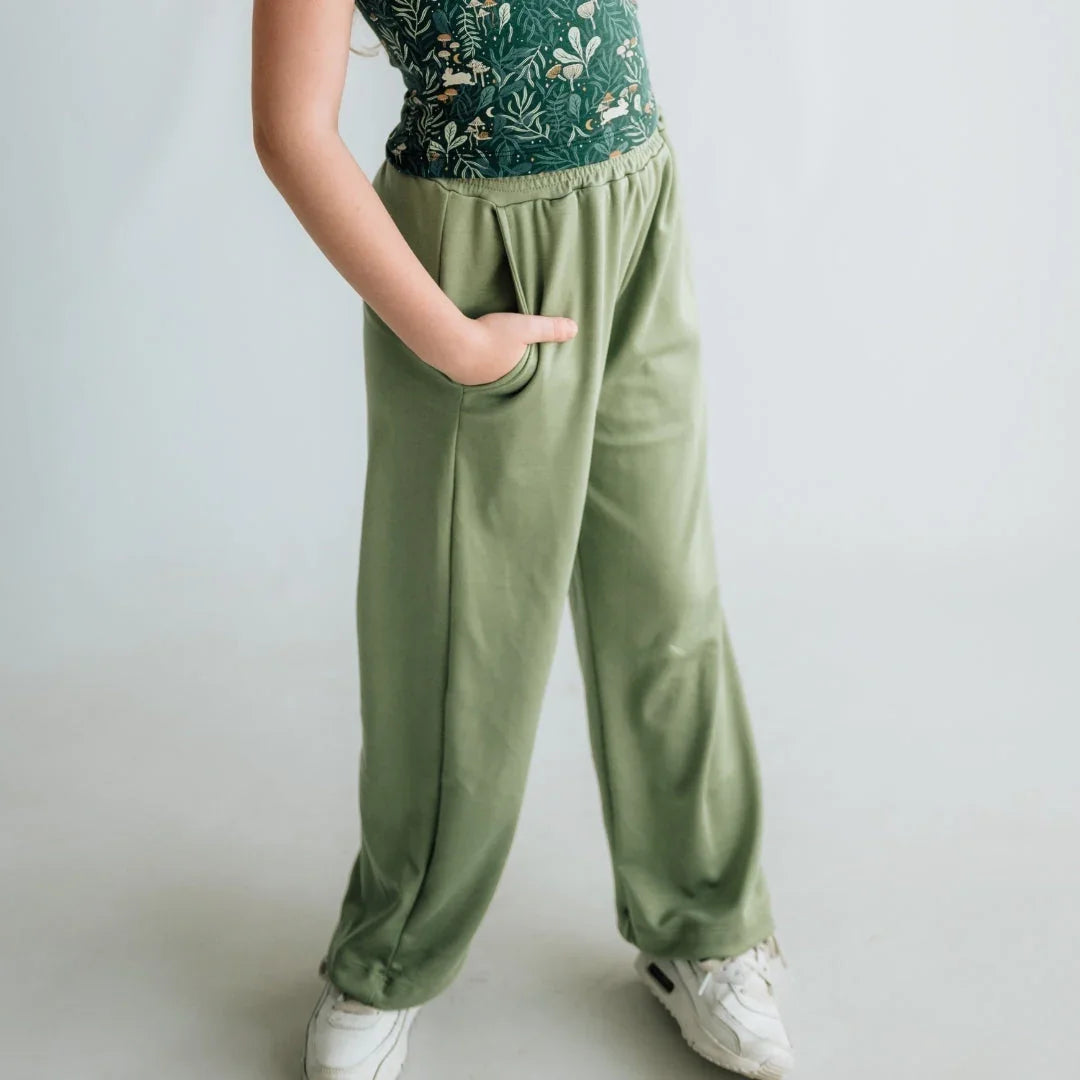 Child wearing sage green pants with pockets, floral top, and white sneakers