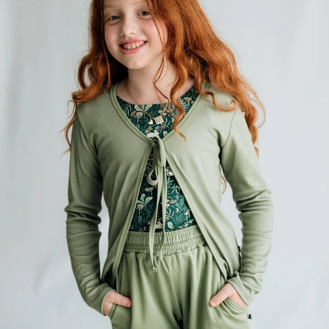 Smiling girl with long red hair in sage green cardigan and pants, floral print shirt