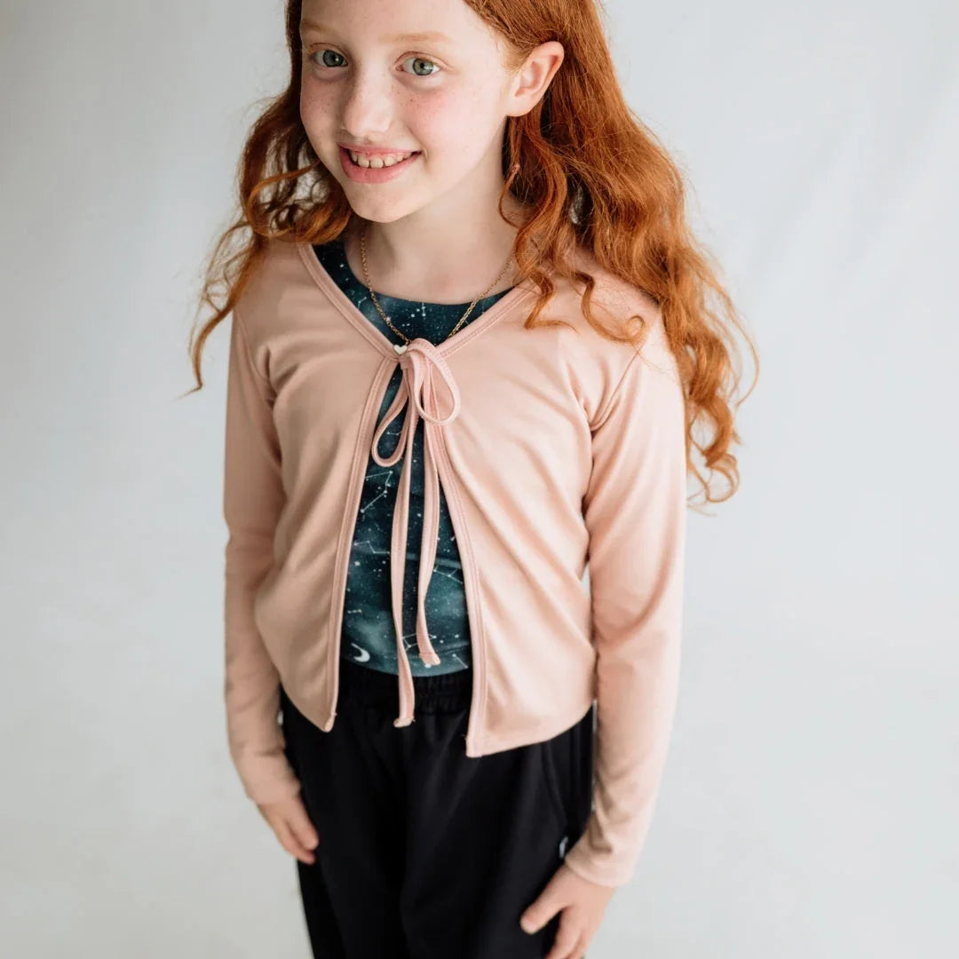 Smiling girl with long red hair wearing a light pink cardigan and black pants
