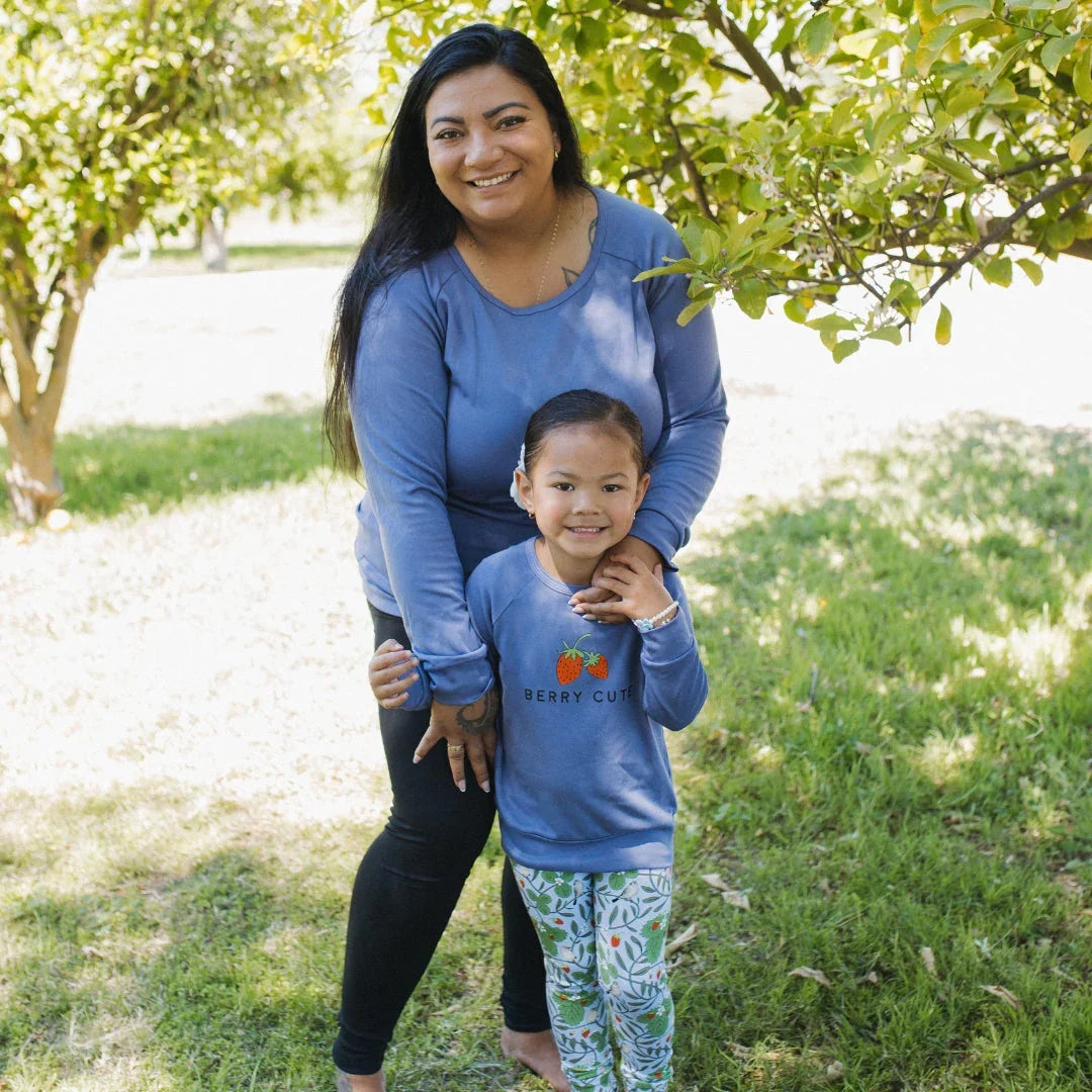 Smiling mother and daughter in matching blue outfits outdoors under green trees