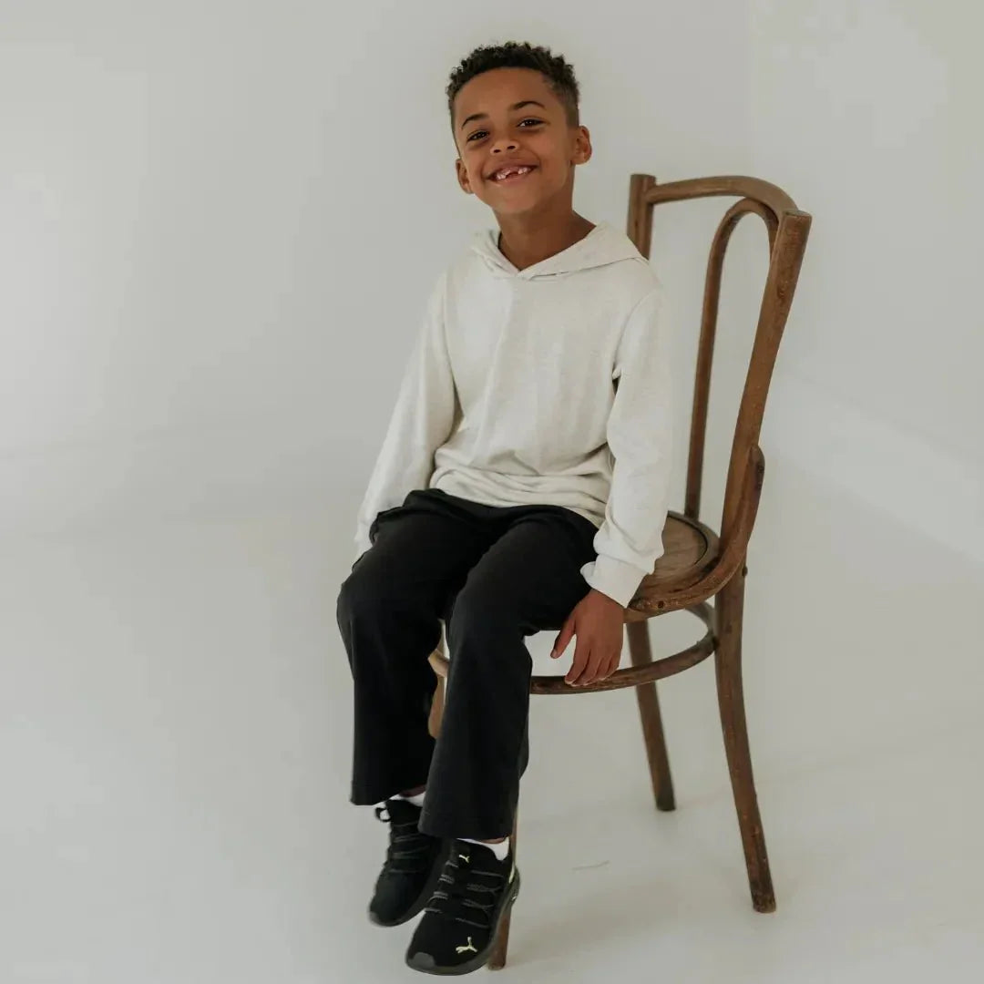 Smiling boy in a lightweight bamboo hoodie and black pants sitting on a wooden chair