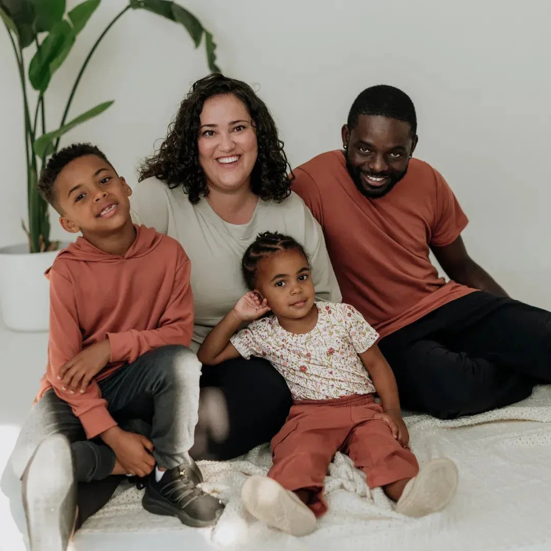 Smiling family in casual bamboo hoodies and pants sitting together on a white rug indoors