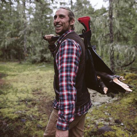 Man outdoors with Zippo Axesaw and firewood in forest, wearing plaid shirt and vest