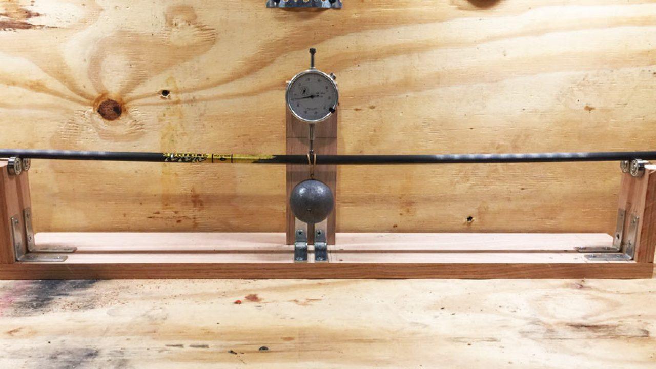 Archery arrow spine tester with gauge on wooden bench for arrow straightness measurement