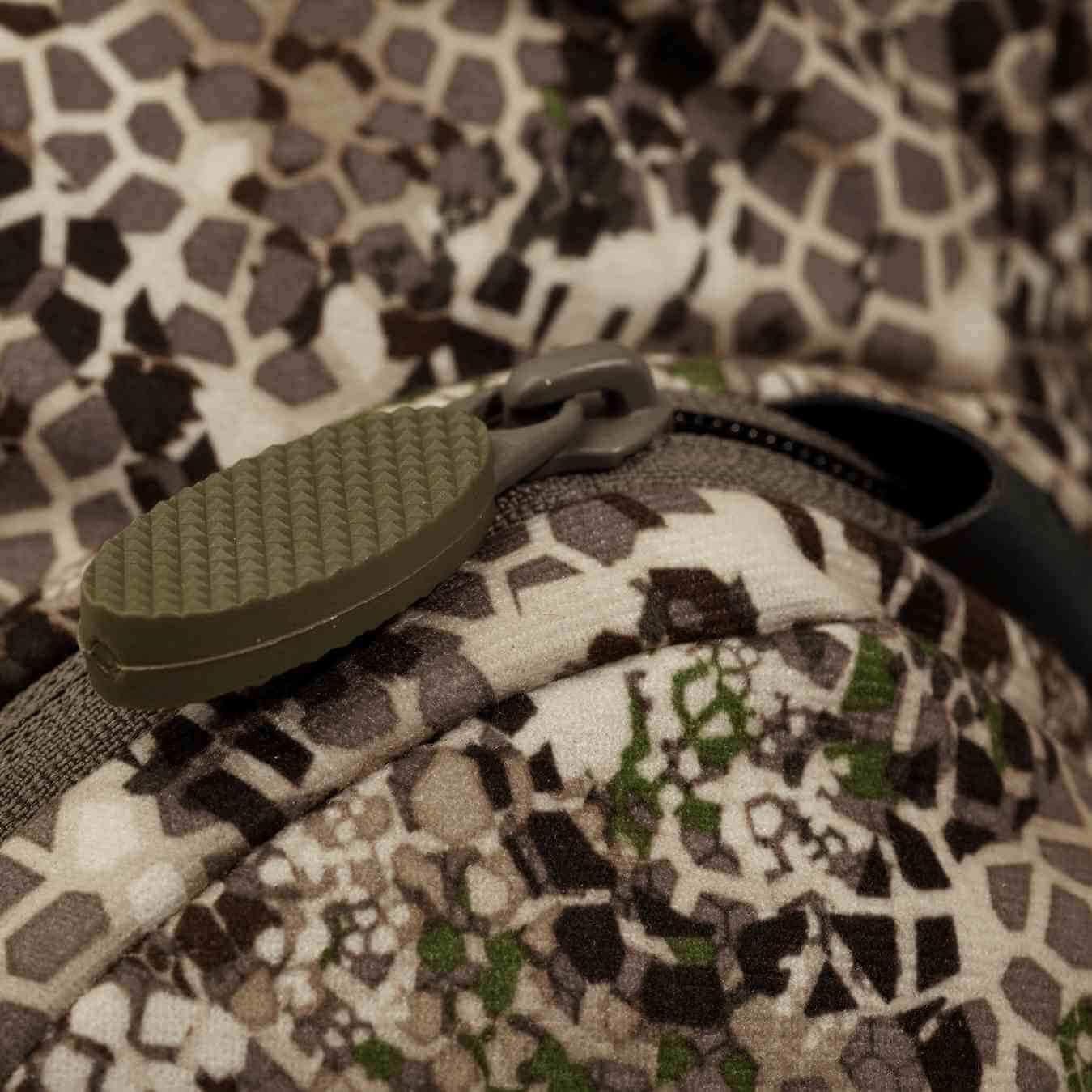 Close-up of camouflage backpack zipper with textured pull tab, outdoor gear detail
