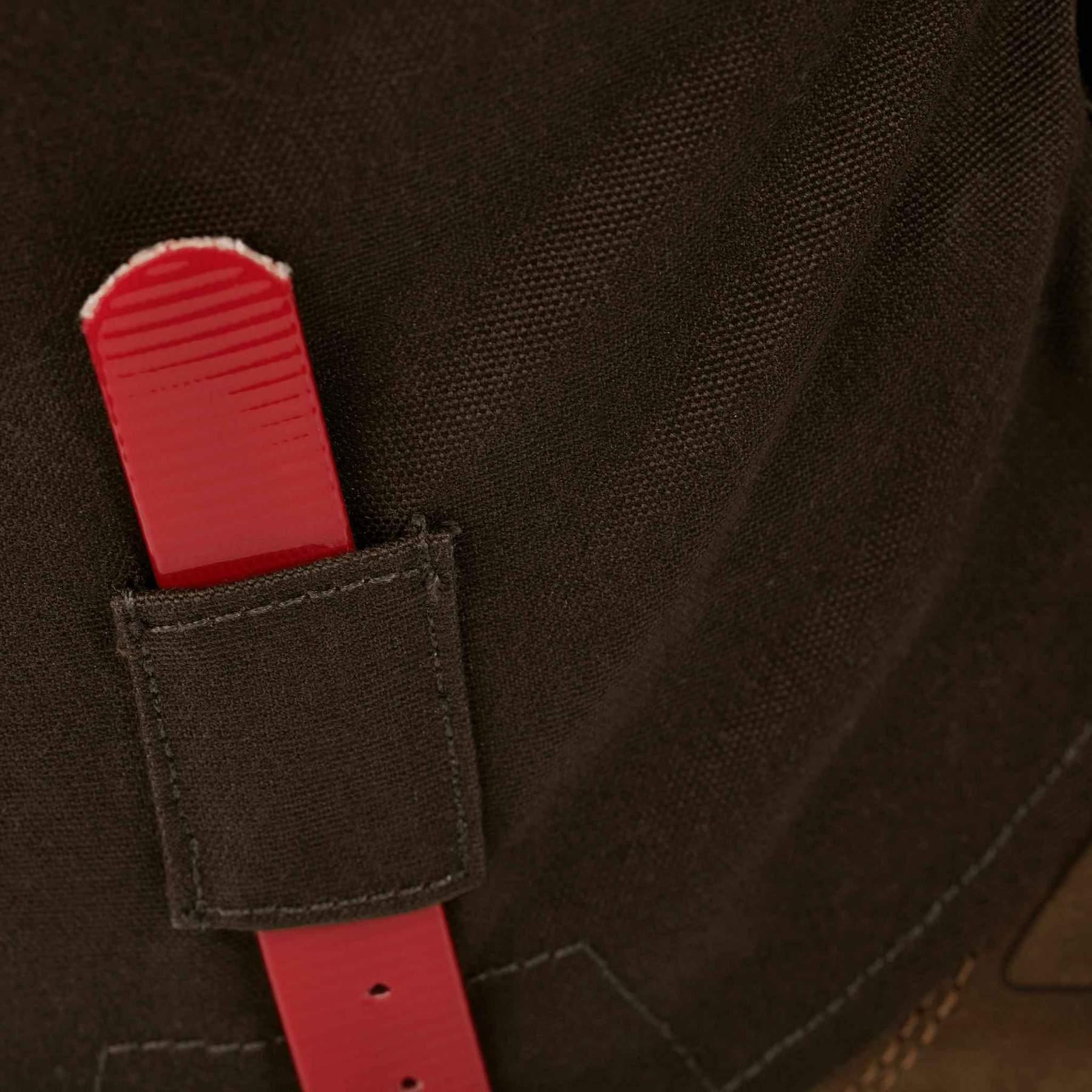 Close-up of black fabric gaiter with red adjustable strap, outdoor gear detail.