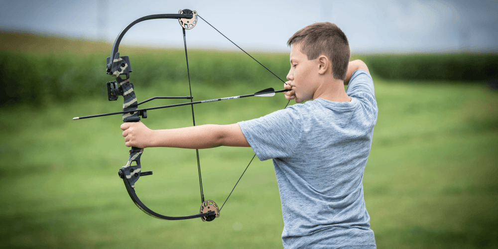 Boy aiming Barnett Tomcat 2 compound bow outdoors on a green field