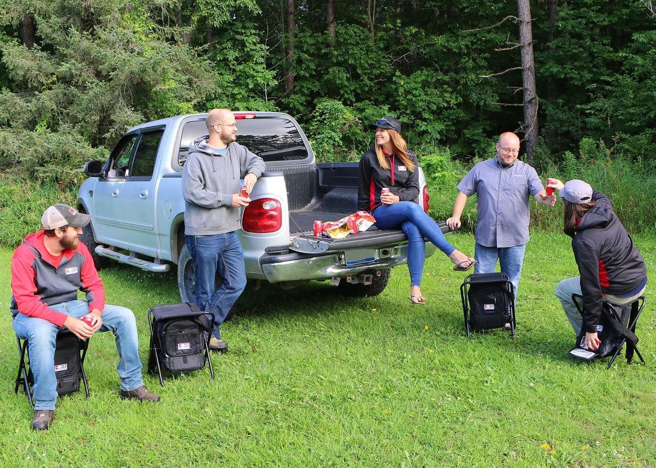 Group of people outdoors with Bohning Archery shooter stools, truck, and snacks in grassy area