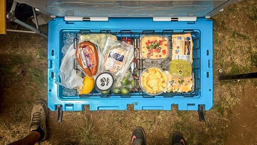Open blue Canyon cooler with food baskets, assorted groceries and snacks outdoors