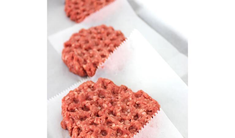 Raw hamburger patties on freezer sheets, separated for storage or grilling prep