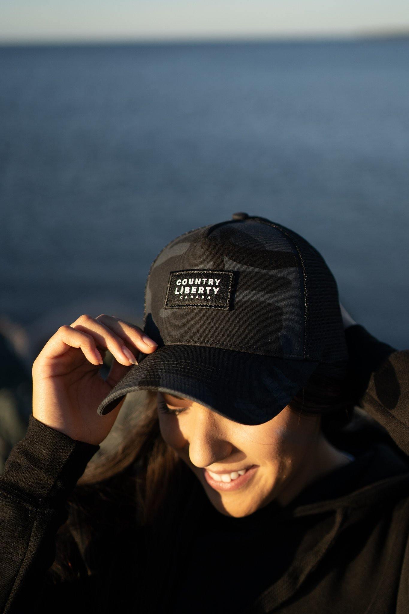 Woman wearing a black camo meshback Country Liberty hat by the water outdoors