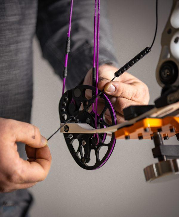 Person adjusting compound bow cam with Hamskea archery rebound dampener indoors