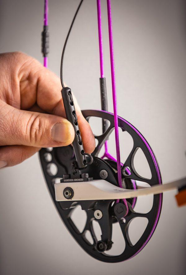 Hand adjusting Hamskea Archery Rebound Dampener on compound bow with purple strings