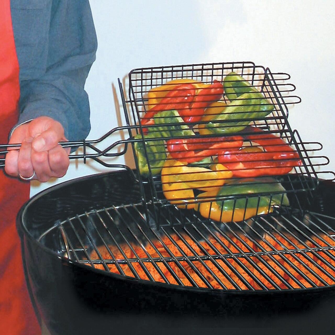 Hand holding grill basket with sliced bell peppers over charcoal barbecue