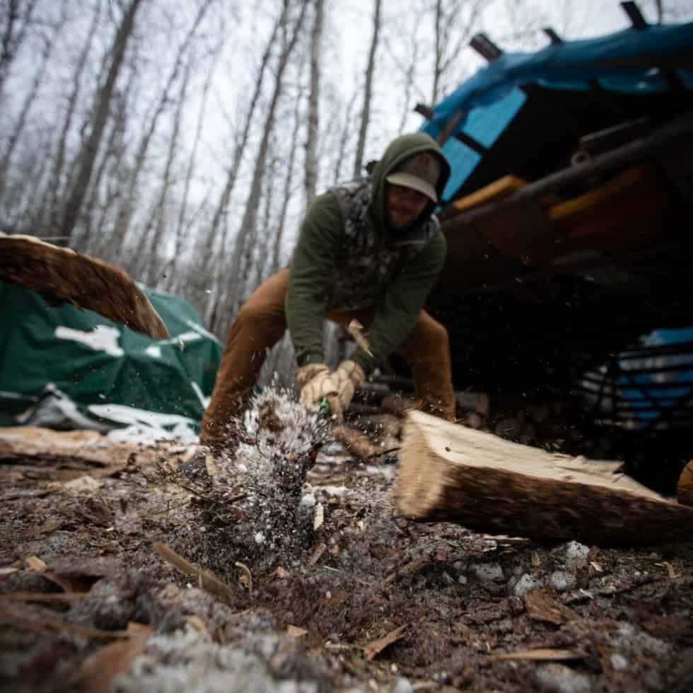 Person chopping wood outdoors with a Hooyman axe in a snowy forest setting