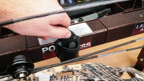 Hand adjusting Last Chance Archery Ready Blade near camo compound bow in archery store