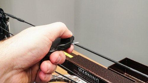 Hand holding Last Chance Archery Ready Blade tool near compound bow string indoors
