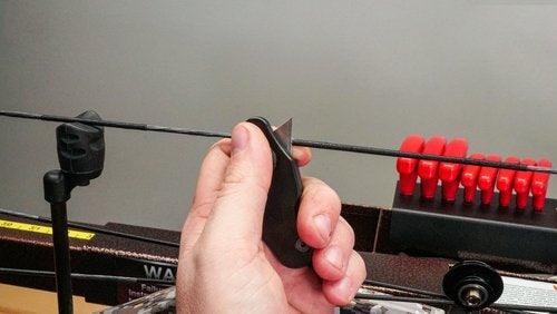 Hand using Last Chance Archery Ready Blade to cut bowstring on archery press