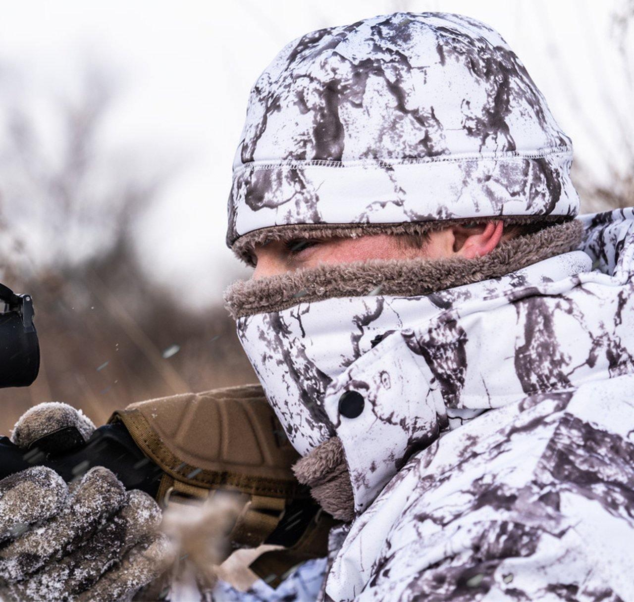 Hunter wearing snow camo neck gaiter and jacket aiming rifle in winter outdoor setting