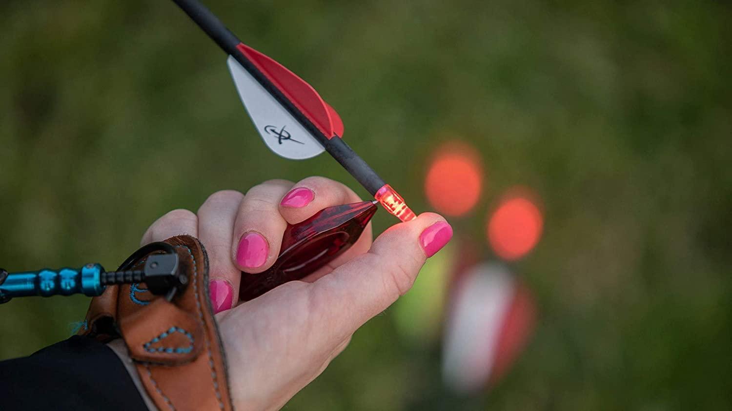 Hand holding lighted Nockturnal universal nock tool with arrow for archery outdoors